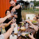 A joyful outdoor gathering with friends clinking glasses over a shared meal.